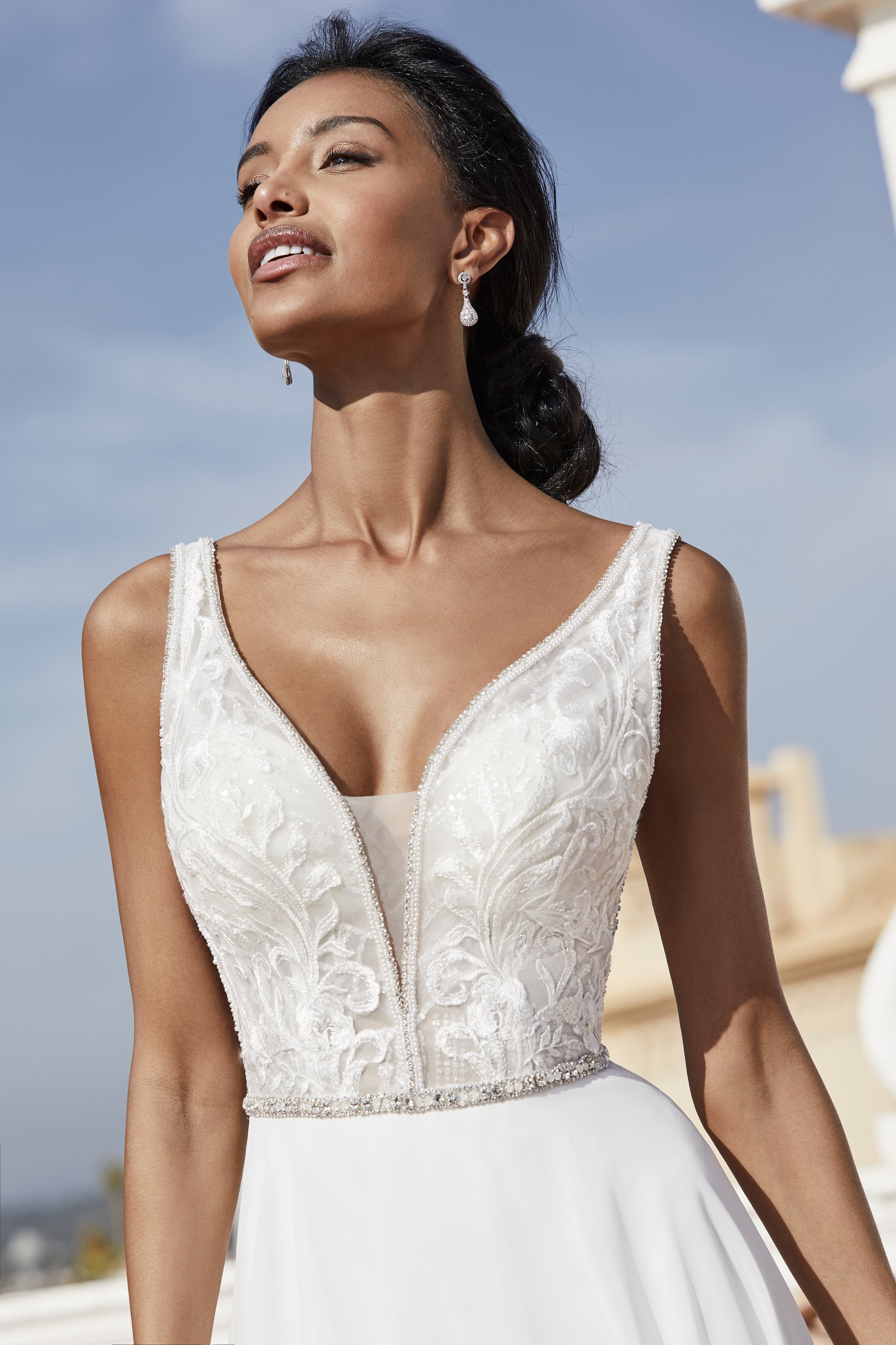 Lady standing outside on patio wearing v-neck wedding dress with illusion plunge neck and embellished belt