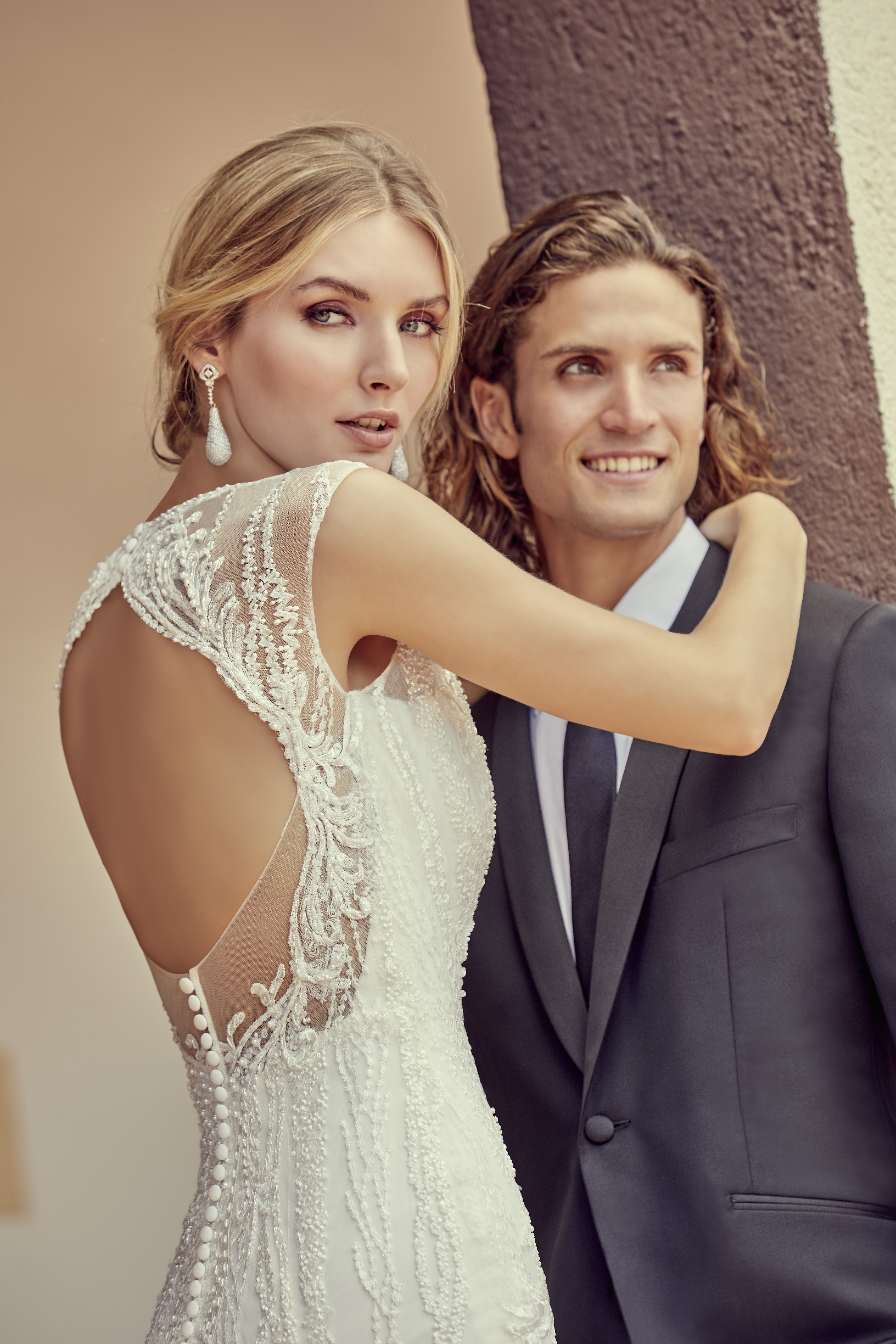 Woman in backless wedding dress with lace appliques hugging man in suit