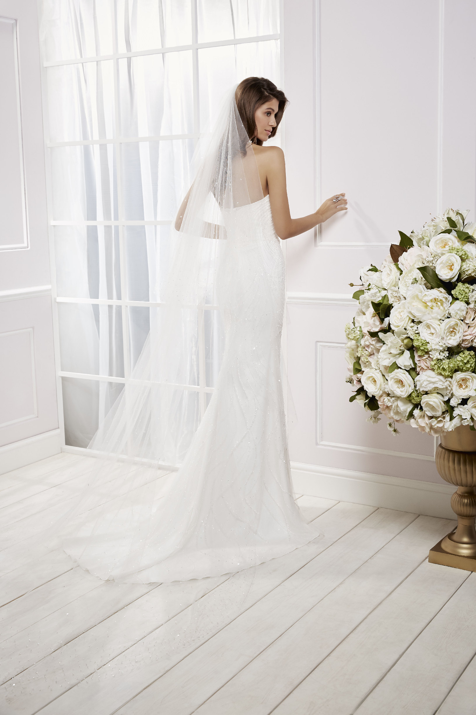 Back image of lady standing in front of window wearing fit and flare wedding dress with floor length bridal veil 