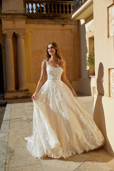 Model stood outside in the sun in Ronald Joyce 69564, a strappy lace ballgown wedding dress with a sparkle tulle skirt and satin waist belt in ivory and light gold