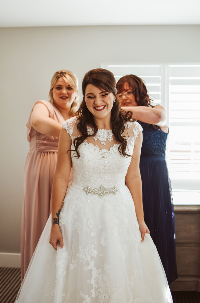 Real bride Sophie stood with her maid of honour and mum in Ronald Joyce 68060, an ivory ballgown wedding dress with a floral illusion neckline, lace and tulle skirt and sparkle belt.