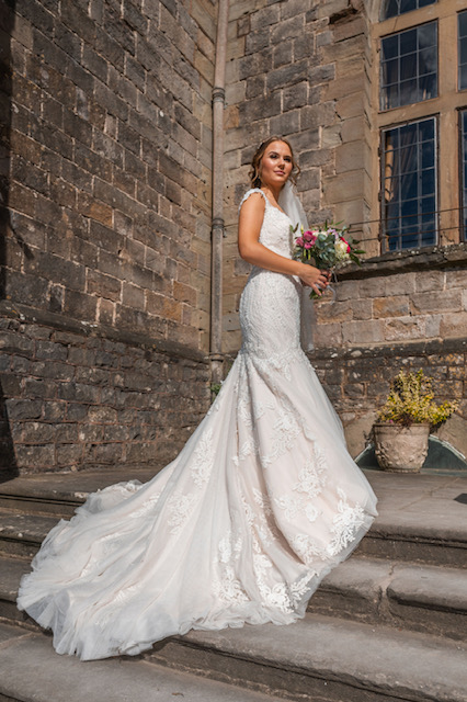 Bride stands outside castle wedding venue wearing fishtail lace and organza wedding dress 