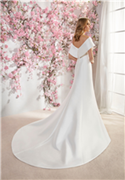 Woman stood against pink floral blossom backdrop wearing mikado fitted wedding dress with v-shaped back detail 
