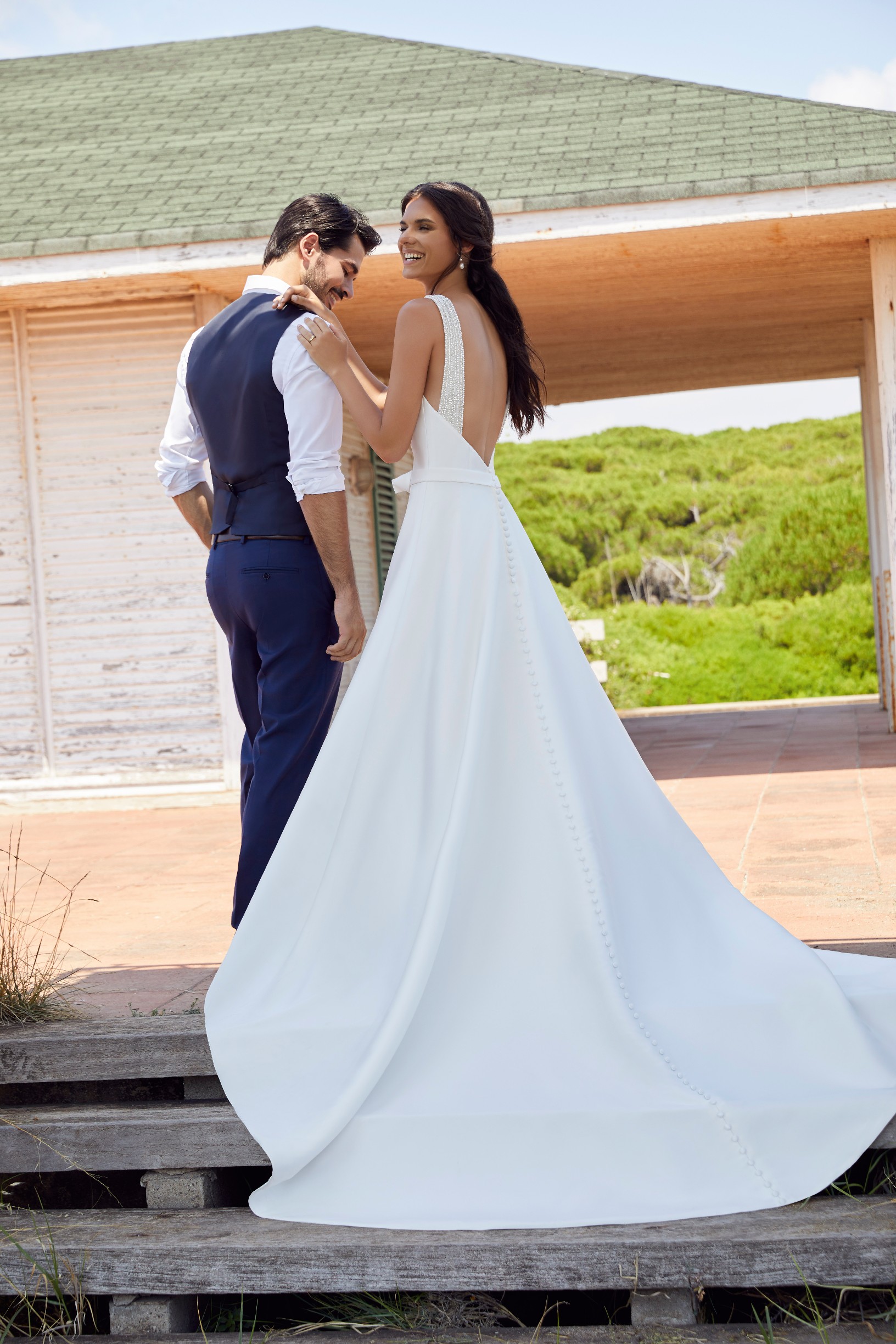 Man standing outside villa with woman wearing low back ballgown wedding dress with beaded straps and belt detail