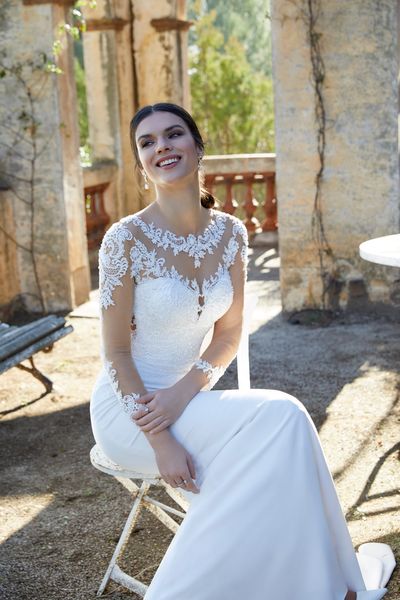 Model sat on an old Spanish terrace wearing Ronald Joyce 18453, a fit and flare wedding dress with long illusion sleeves and a matching sweetheart neckline