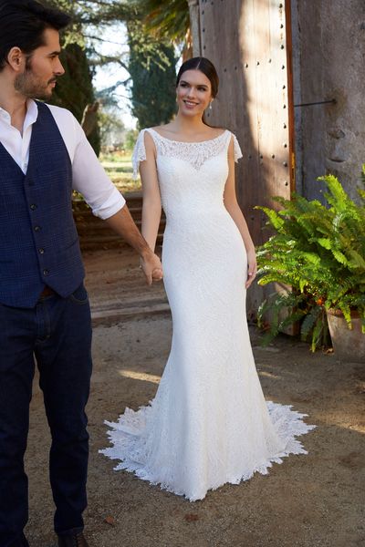 Model stood with a groom by an open gate in Ronald Joyce 18455, a plain fit and flare wedding dress with lace tie shoulders, a sweetheart lace illusion neckline and lace hem