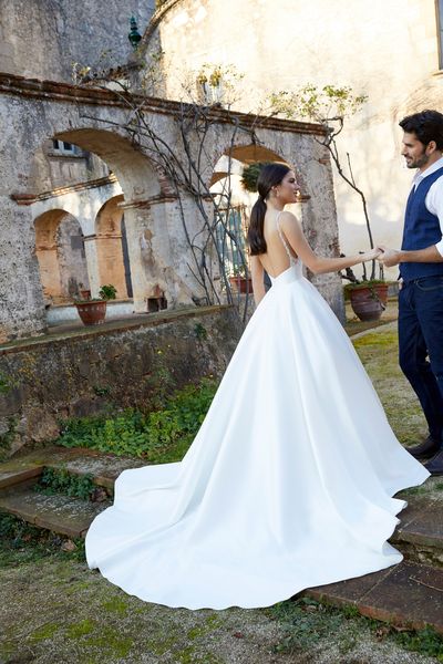 Man standing in garden with woman wearing ballgown wedding dress showing the back of dress and train