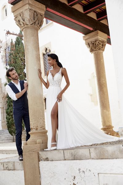 A black model stood outside by a column in Victoria Jane style 18552, a destination A-line wedding gown with thigh split, beaded strappy body and plain chiffon skirt.