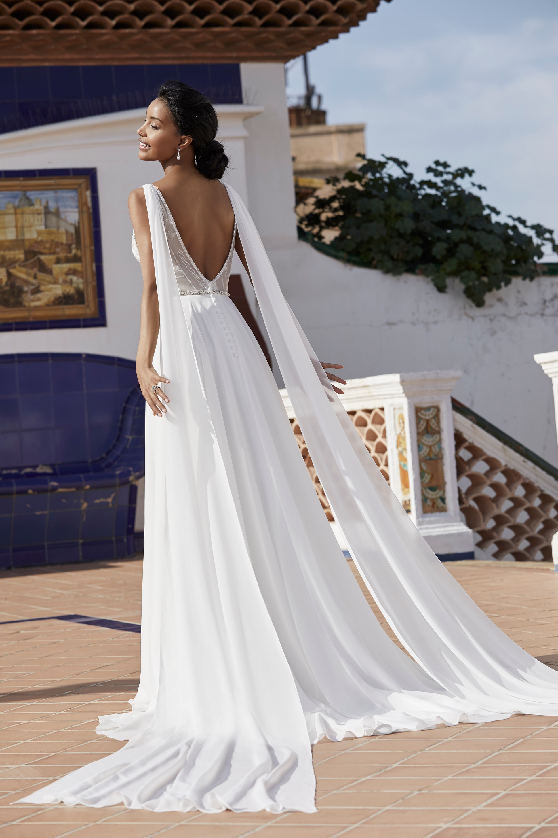 Lady standing outside in the sun on terrace wearing backless wedding dress with drape shoulder detail 