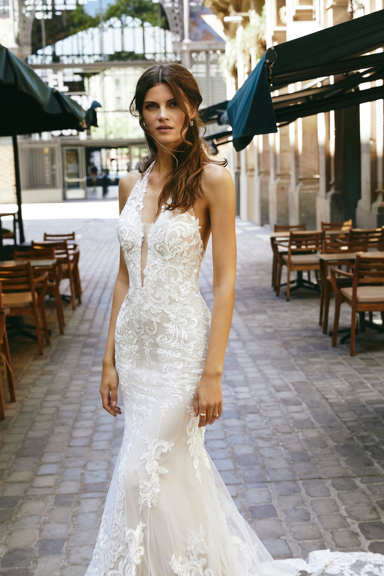 Woman standing in street between parasols wearing lace and tulle fit and flare wedding dress with lace applique detail