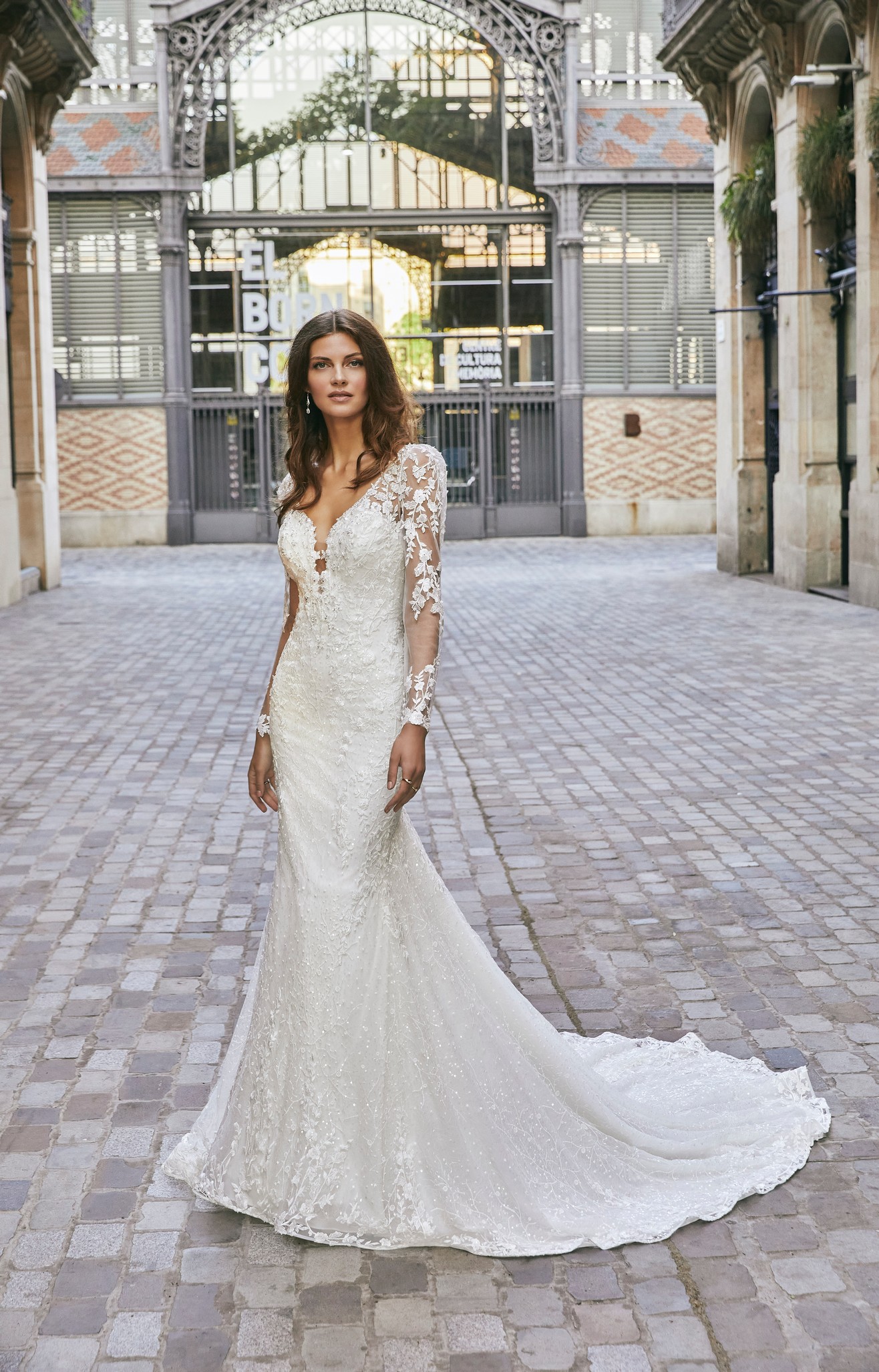 Lady standing in plaza wearing fit and flare wedding dress with illusion long sleeves and sweetheart neckline