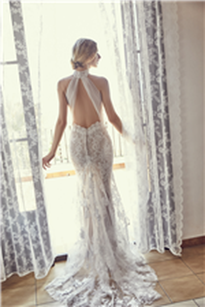 Lady standing in window wearing lace, backless wedding dress with tulle strap detail