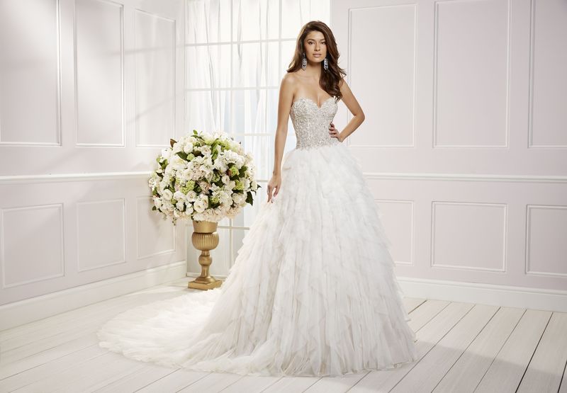 Brown haired lady standing in front of window and white panelled room wearing heavily beaded strapless ballgown wedding dress and long statement earrings