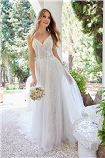 Bride stood near trees in Ronald Joyce 69514, a jersey and lace sheath wedding dress with a v-neckline and spaghetti straps. Model also wears a tulle overskirt for two looks.