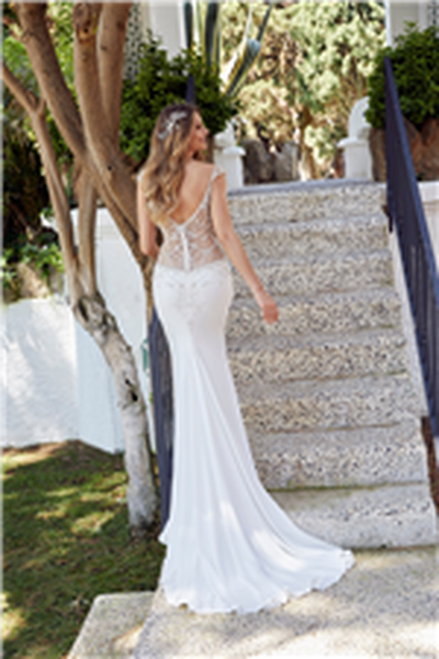 Blonde woman standing in front of garden steps wearing sheer beaded bodice wedding dress with contrasting plain crepe skirt