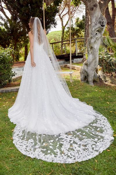 Lady standing next to tree swing in garden wearing princess ballgown wedding dress with cathedral length matching veil