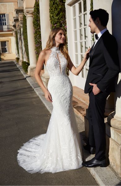 Woman wearing fit and flare wedding dress with high neckline and keyhole detail standing outside looking at man in a suit