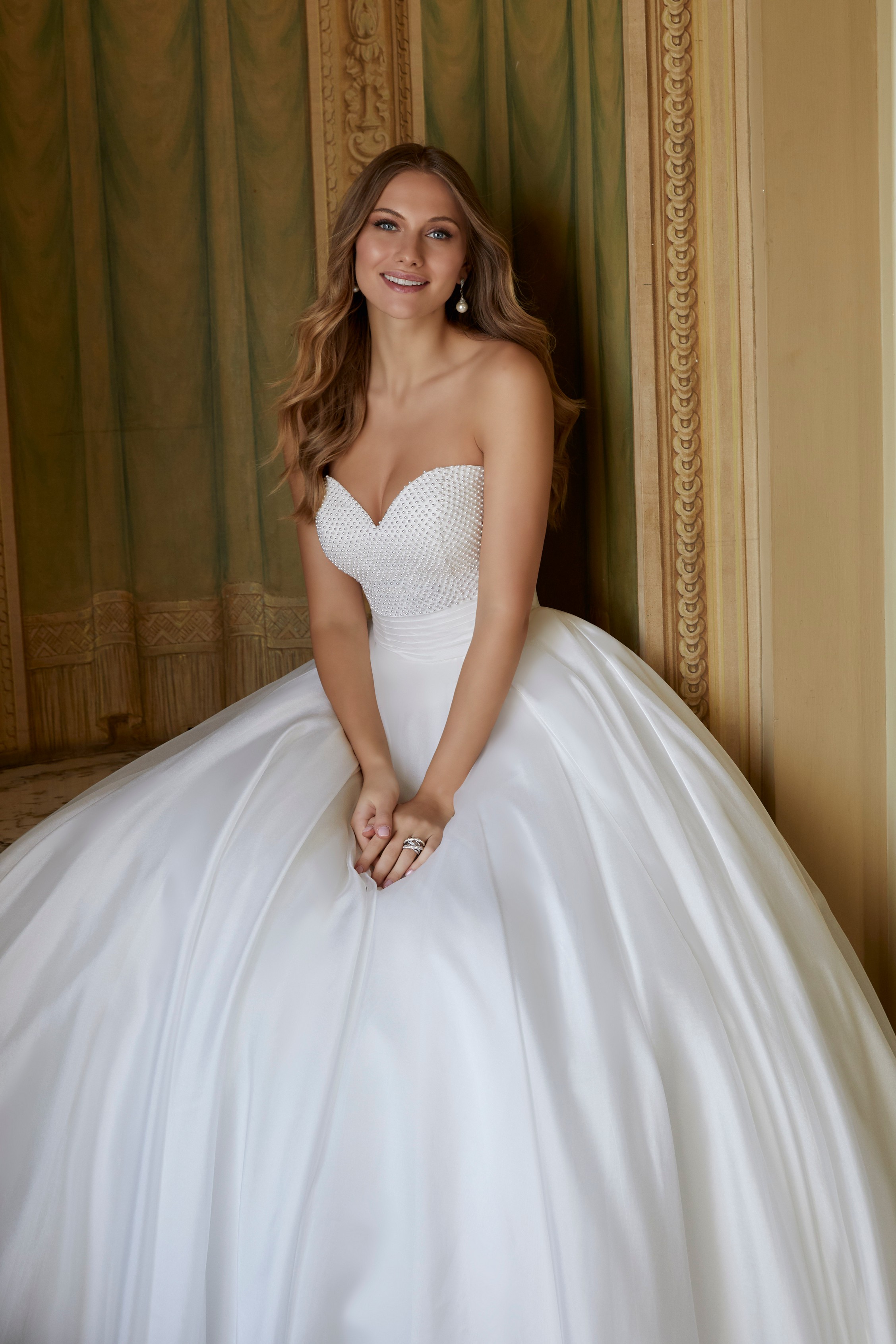 Close up of model sat down in Ronald Joyce 69559, a strapless version of the ballgown wedding dress with a pearl beaded sweetheart bodice and a ruched waistband.