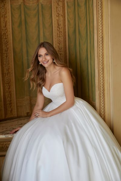 Blonde woman sitting in front of patterned wall wearing strapless beaded ballgown wedding dress 