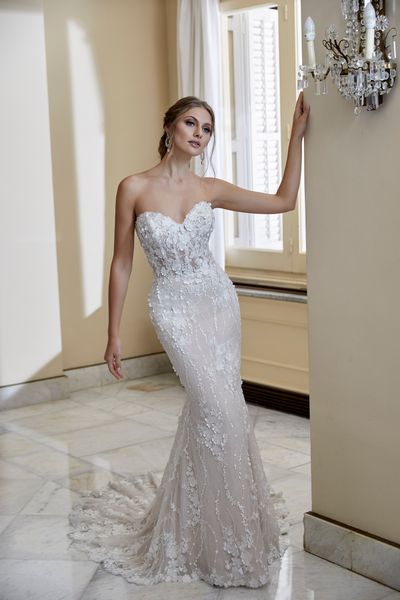 Model stood in a grand room by a wall chandelier in Ronald Joyce 69566, a strapless floral applique fit and flare wedding dress with a sweetheart neckline 