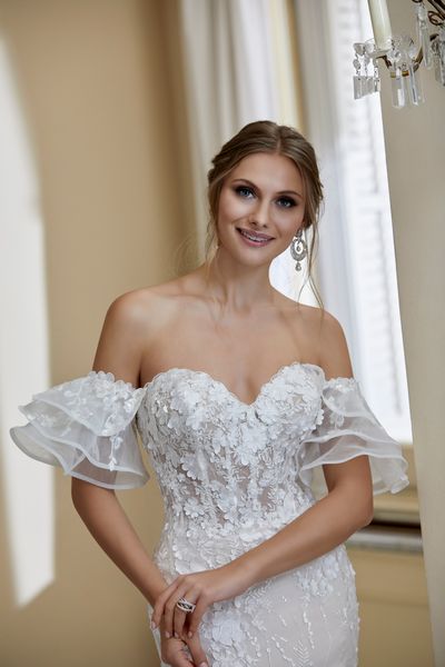 Model in Ronald Joyce 69566, a strapless fit and flare wedding dress with delicate floral appliques, a sheer bodice and sweetheart neckline. Model wears detachable arm cuffs.