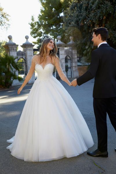 Woman wearing princess style ballgown wedding dress with beaded bodice and 3/4 length sleeves holding hands with man in suit