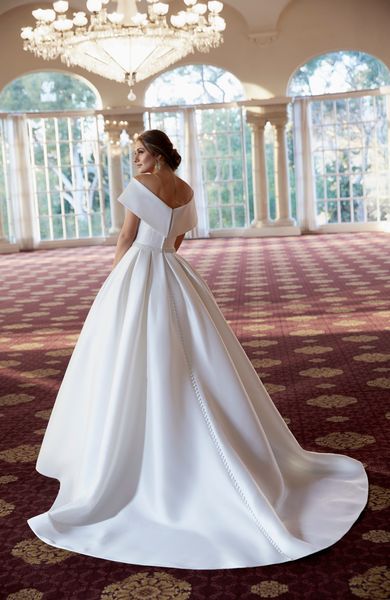 Back image of woman standing in ballgown wedding venue wearing simple and classic princess ballgown wedding dress with low off the shoulder back detail