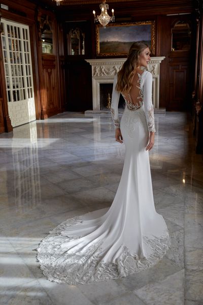 Lady standing in ballgroom venue wearing crepe wedding dress with lace applique sleeve and illusion back