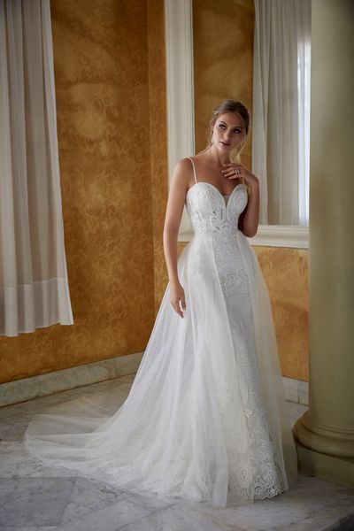 Model stood by a pillar in an empty room wearing Ronald Joyce 69578, a strappy lace two in one wedding gown with a sweetheart neckline and plain tulle A-line overskirt.