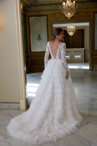 Back of a model wearing Ronald Joyce 69584, a glamorous ivory winter wedding dress featuring a lace illusion bodice, long lace sleeves, a feather skirt and necklace back