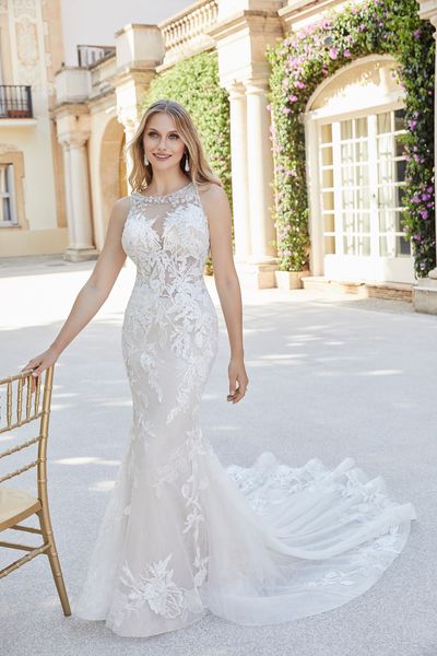 Woman standing outside chateau villa leaning in gold chair wearing fit and flare lace and tulle wedding dress with high illusion neckline