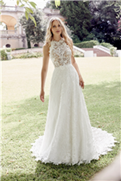 Model stood on a sunny lawn in Ronald Joyce 69606, a stunning boho wedding dress with a sheer lace bodice, floral applique halter neck and lace A-line skirt with a scalloped hem 
