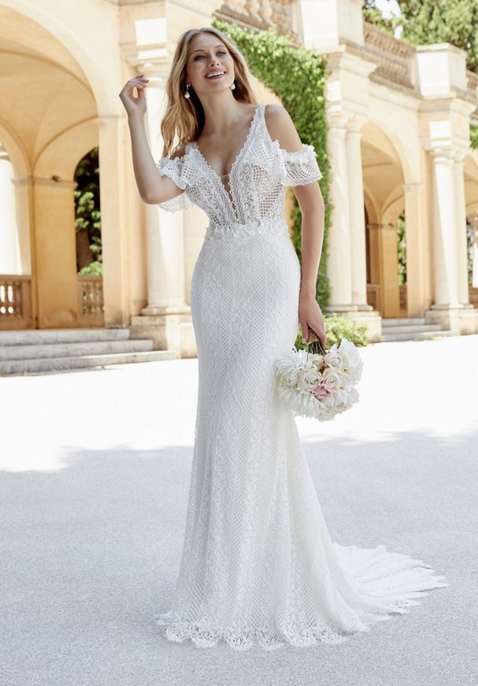Model stood in an Italian courtyard in Ronald Joyce 69607, a lace fit and flare boho wedding dress with a plunging neckline, straps and detachable cuffs for a cold shoulder look.