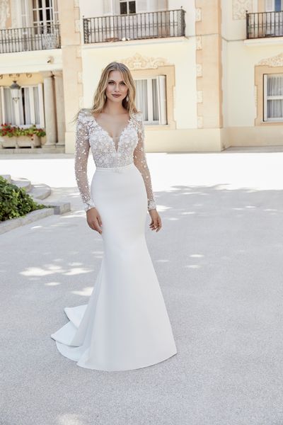 Model stood outside Italian apartments in Ronald Joyce 69609, a fit and flare wedding gown with a plain skirt and striking bead and floral applique bodice with long sleeves.