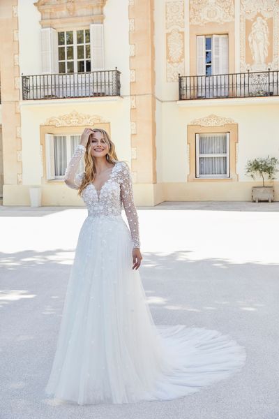 Model stood by sunny apartments in Ronald Joyce 69609, a fit and flare wedding gown with a plain skirt and beaded applique bodice. Model wears a sparkly tulle overskirt for two looks