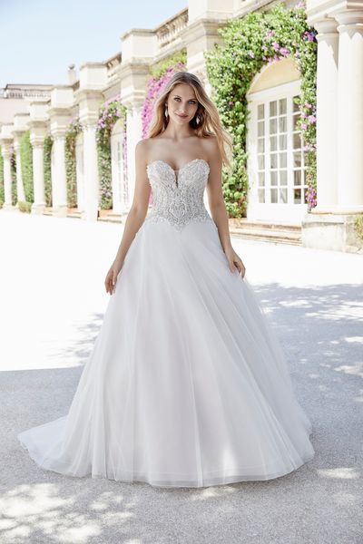 Blonde model stood on a pink floral terrace in Ronald Joyce 69612, a strapless ballgown wedding dress with a crystal and pearl-beaded sweetheart bodice and plain tulle skirt