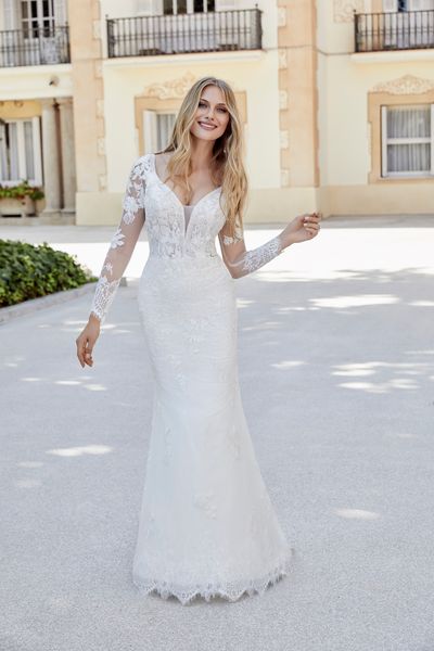 Model stood by sunny Italian apartments in Ronald Joyce style 69613, one of our lace fit and flare wedding gowns with long sheer lace sleeves, a plunging illusion neckline and eyelash hem