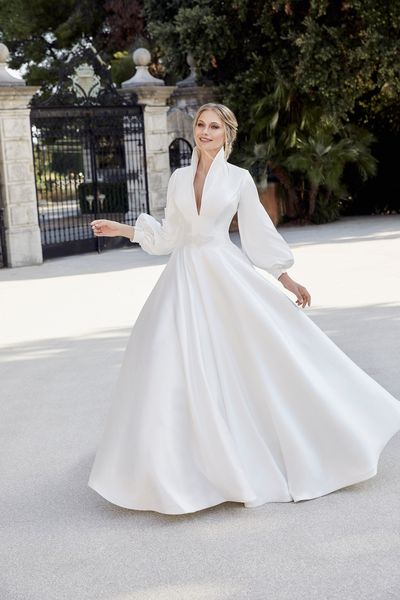 Woman standing in front of gates and garden wearing mikado ballgown wedding dress with distinctive collar detail 