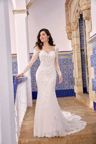 Model stood in a blue pattern tiled Italian hallway in Ronald Joyce 69667, a long sleeved wedding dress with lace appliques, a sweetheart neckline and sheer sleeves.