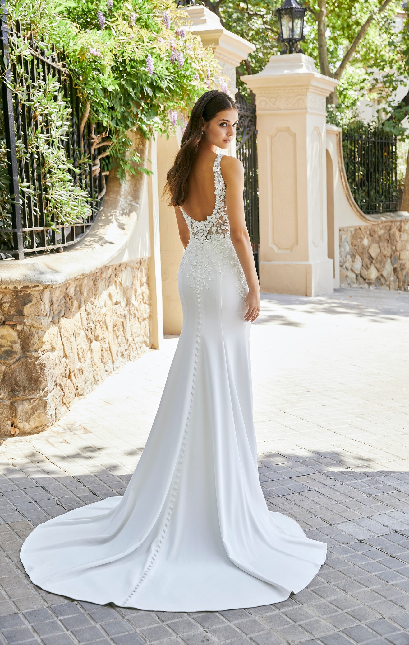 lady standing on street in Barcelona in front of gates wearing fitted crepe wedding dress with low back and button detailing