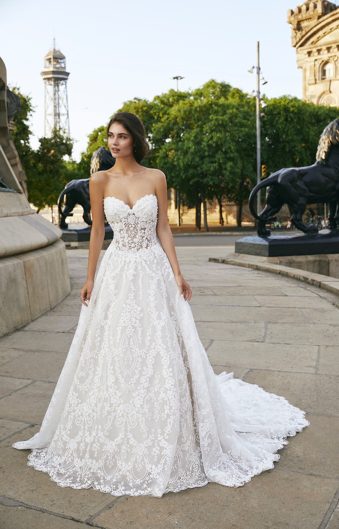 Model stood outside in a quiet street in Ronald Joyce style 69709, a strapless lace A-line wedding dress with a sweetheart neckline and illusion bodice. 