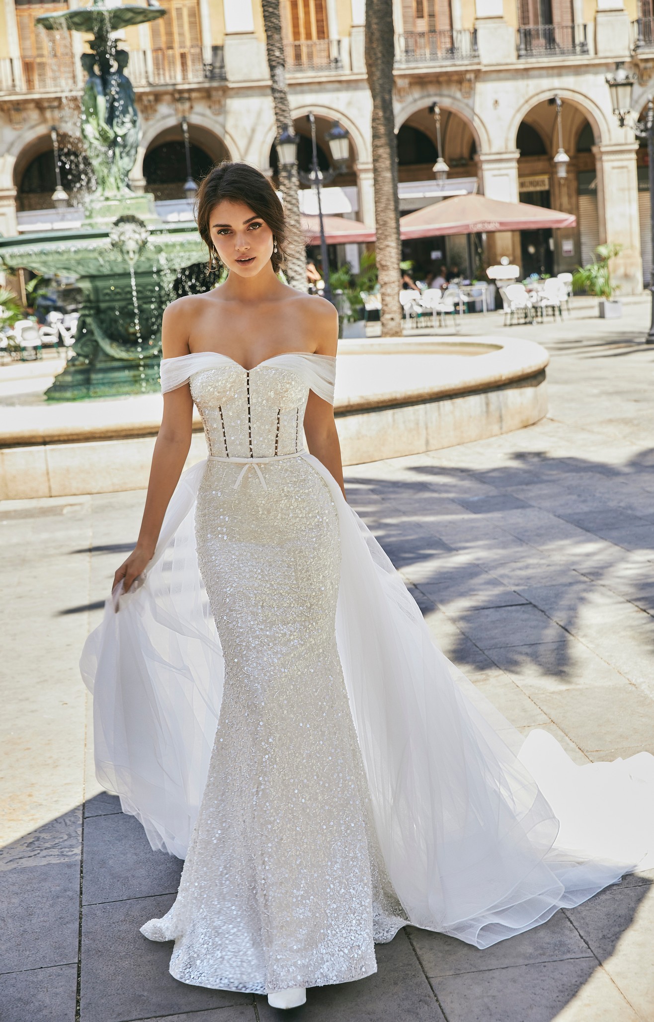 Front profile of model wearing Ronald Joyce wedding dress style 69722, an off the shoulder pearl-beaded fit and flare wedding dress