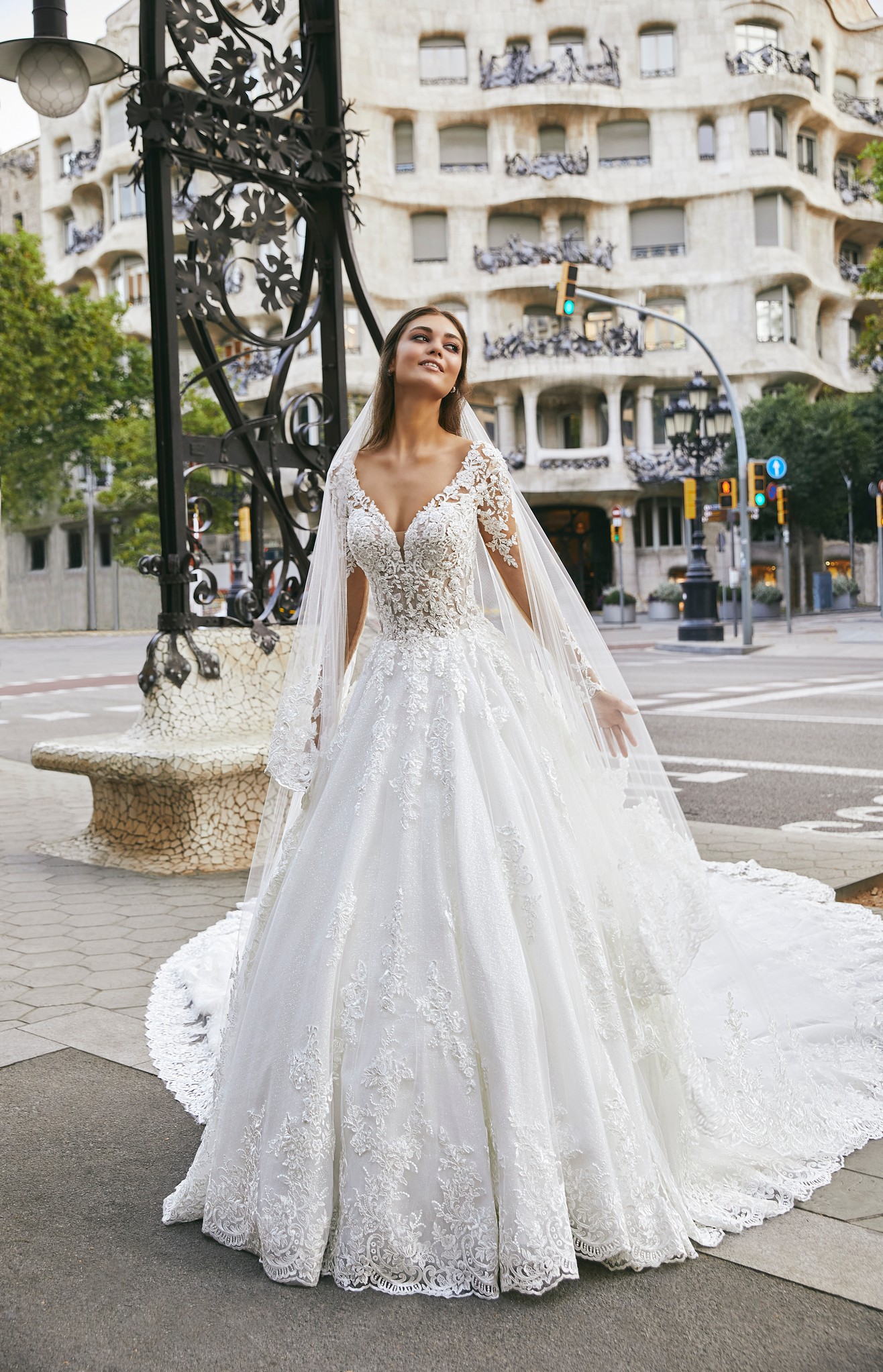 Woman standing on street in Barcelona wearing princess ballgown lace wedding dress with long illusion sleeves and plunging v-neckline
