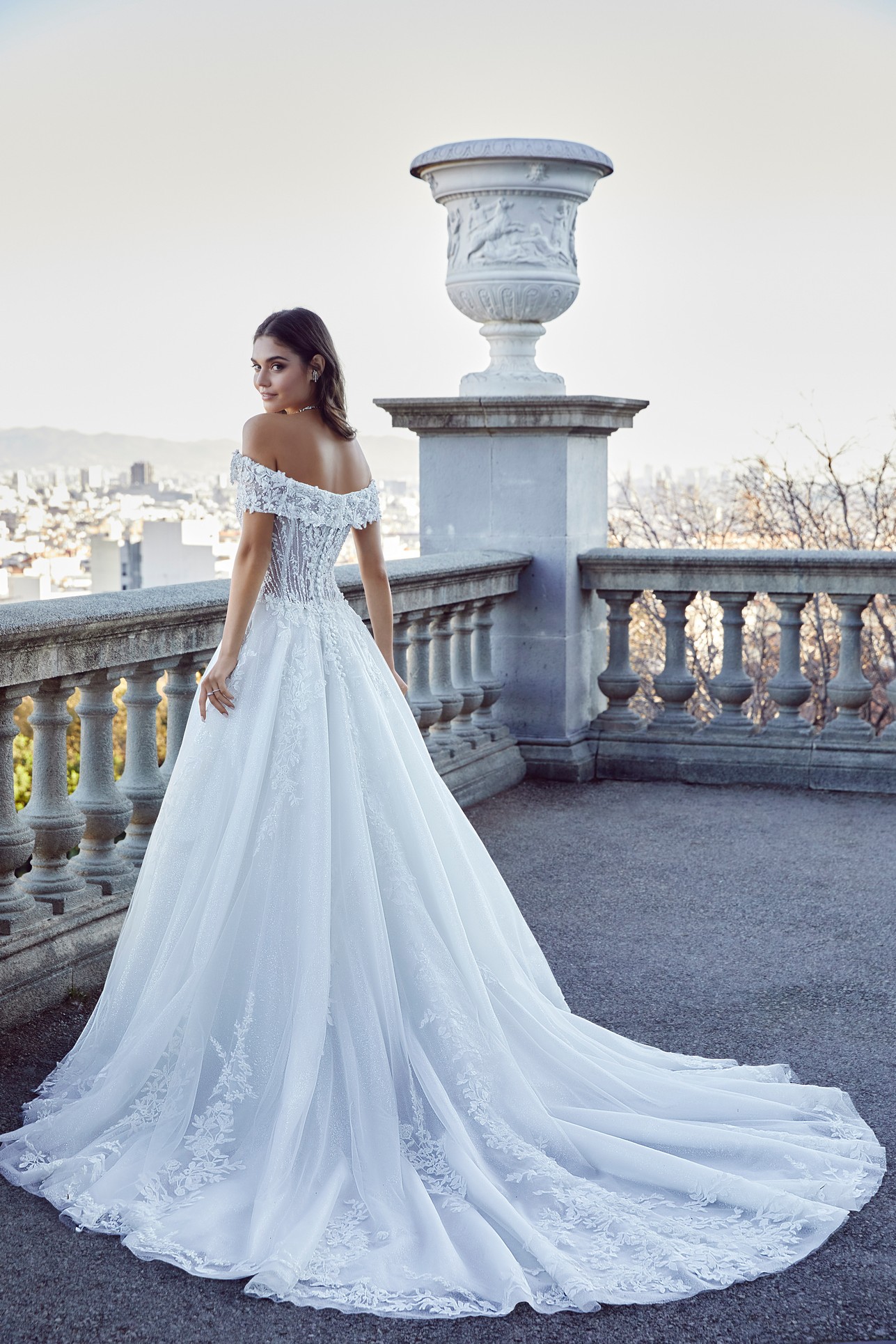 Back image of woman in white ballgown dress standing in front of city view 