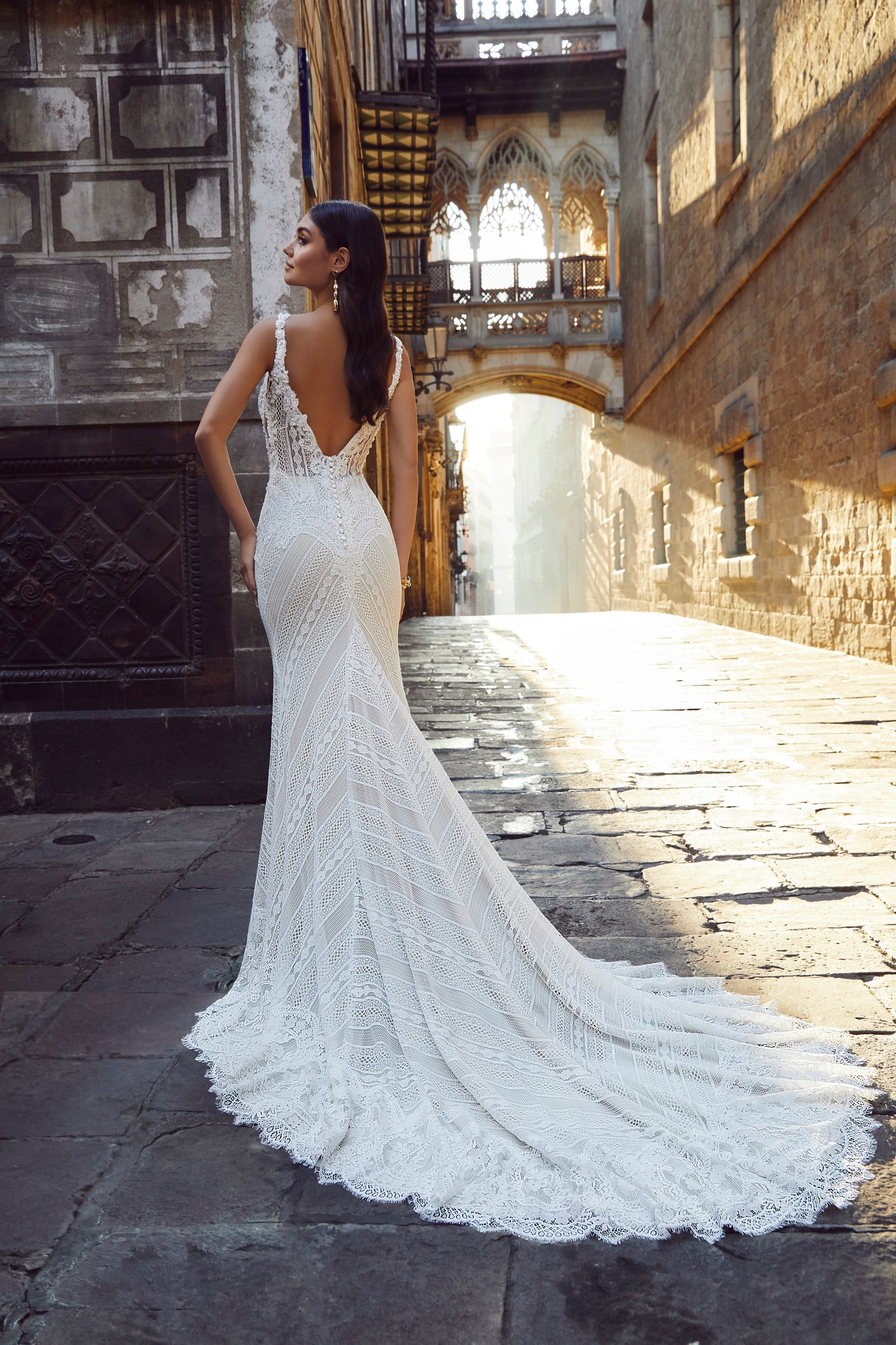 back image of woman wearing lace bohemian wedding dress standing in street 