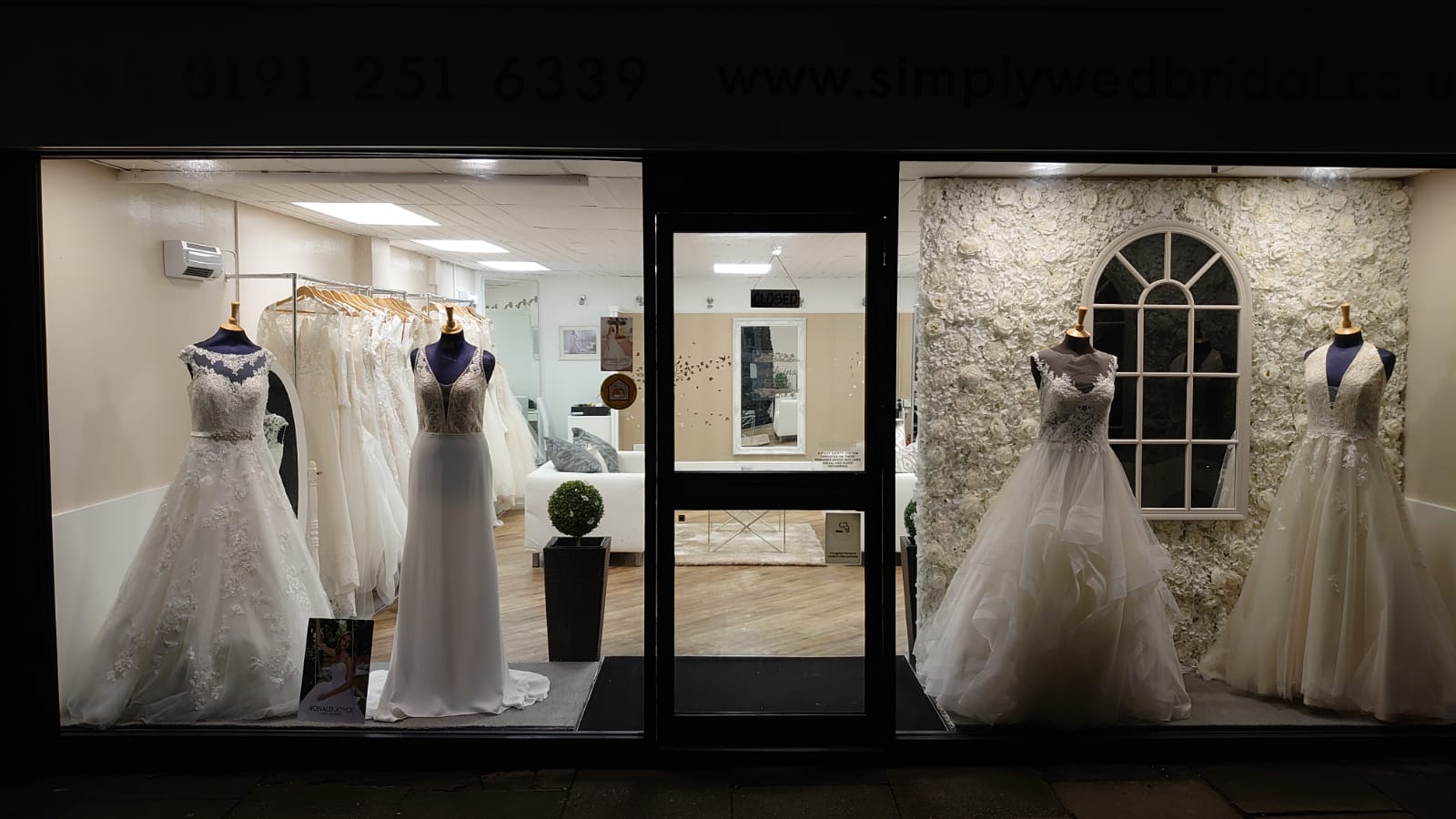 Newcastle's Simply Wed bridal shop window display lit up at night to show four ivory wedding dresses on black mannequins
