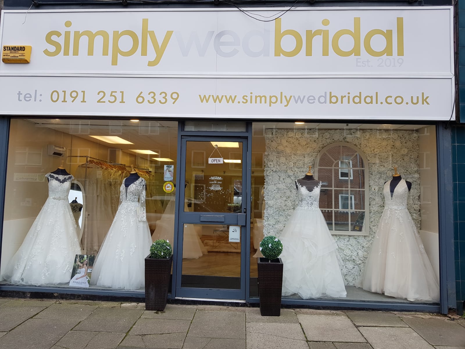 Newcastle's Simply Wed Bridal shop sign and window display showcasing four ivory wedding dresses on black mannequins. 