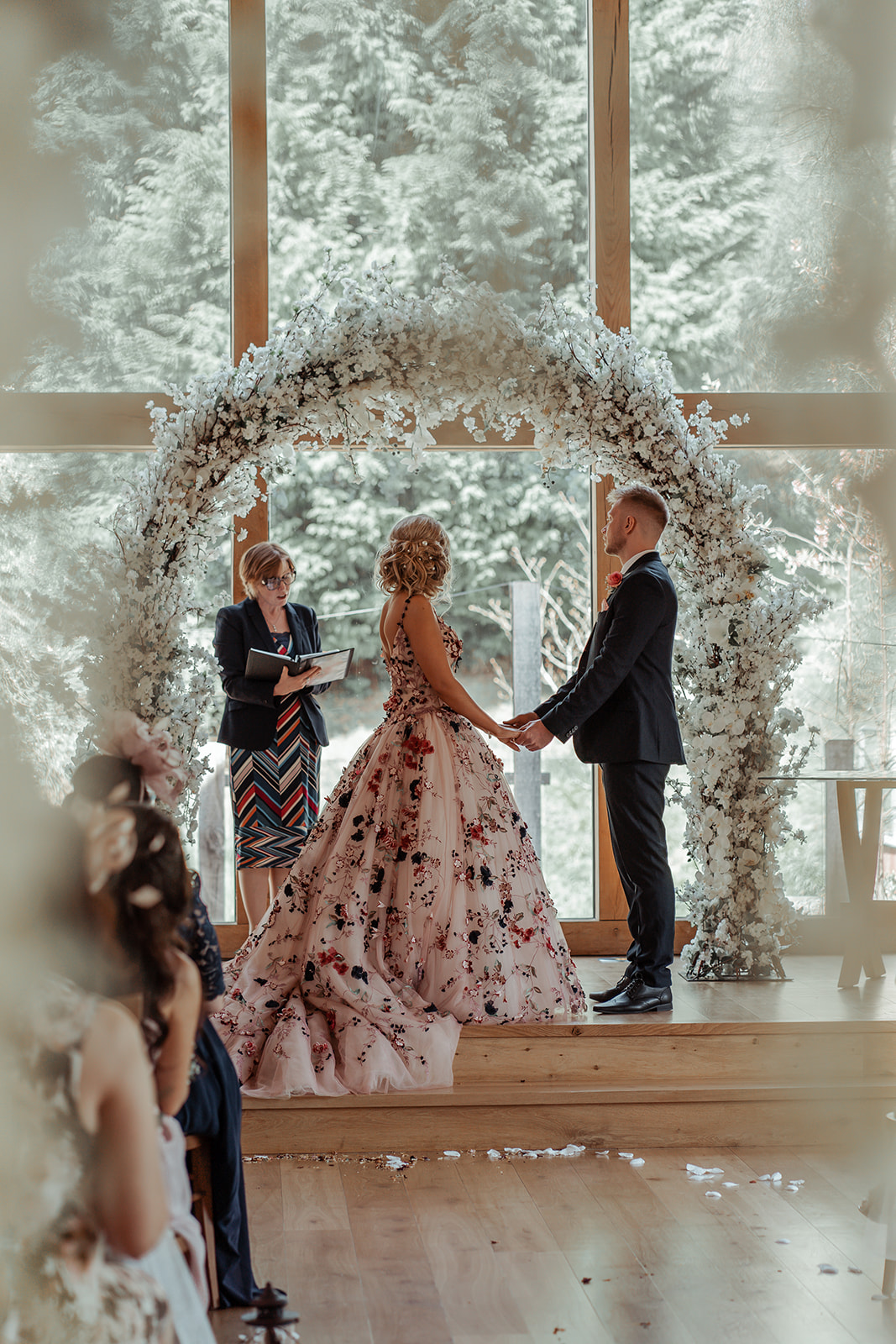 Ronald Joyce real bride, Rebecca, and her husband, Michael, holding hands while saying their vows in front of the registrar. Rebecca has curled blonde hair and wears our blush coloured Celestina ballgown wedding dress.