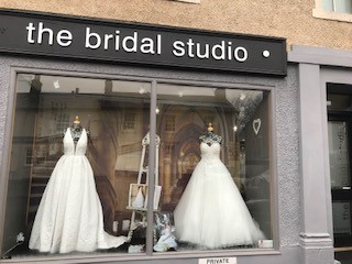 Photo of two ivory wedding dresses displayed in the shop window at The Bridal Studio in Dollar in Scotland. One dress has a plunging halterneck and one has a sweetheart neckline