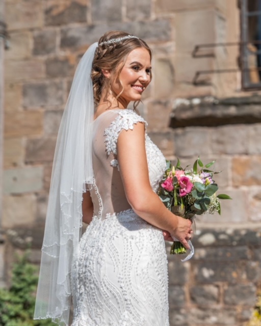 Back image of bride on wedding day wearing fitted dress with illusion back with lace detail 